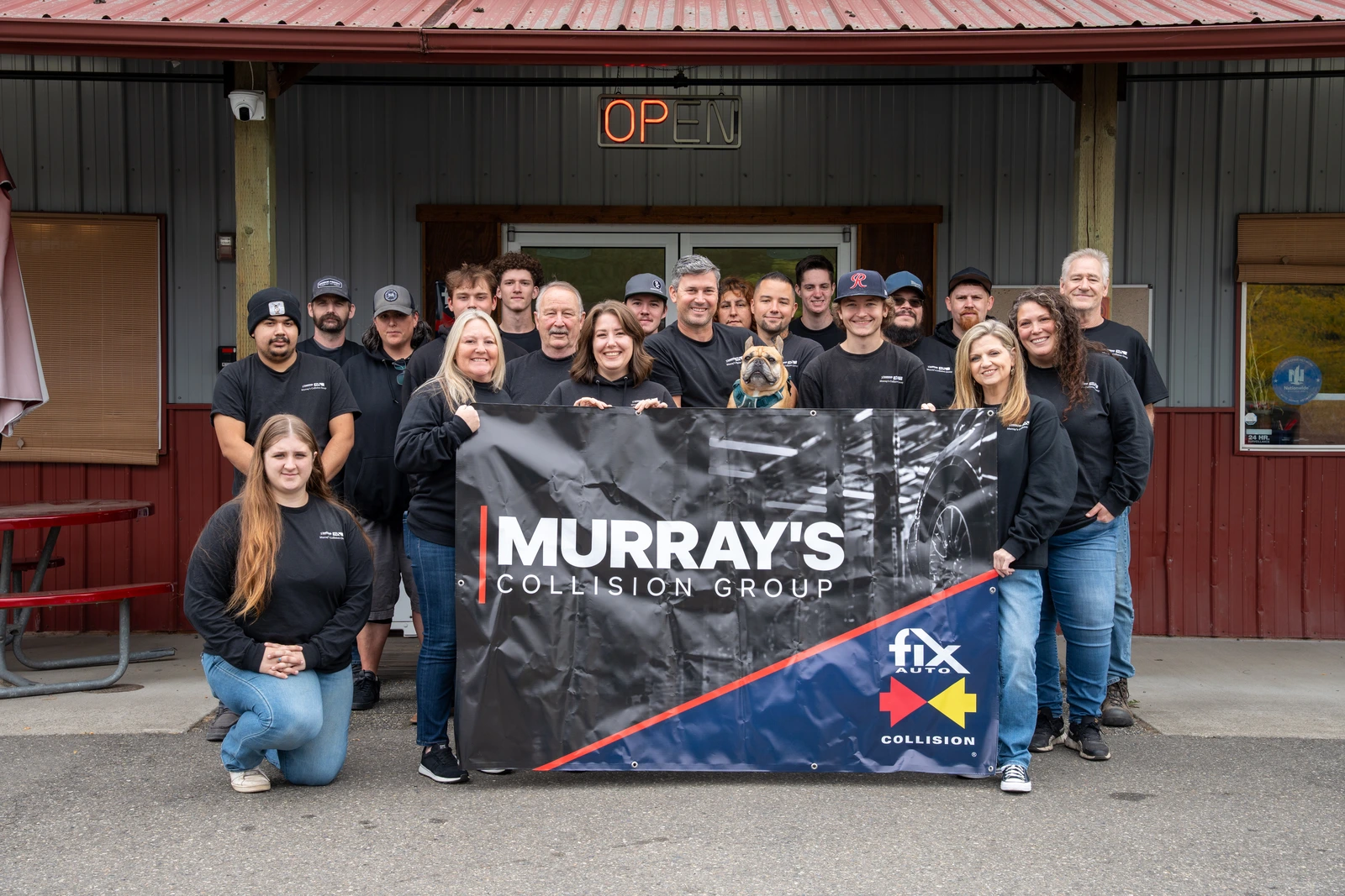 The Murray's Collision Group team and the shop dog holding a Murray's Collision Group and Fix Auto Collision banner outside one of the group's shops